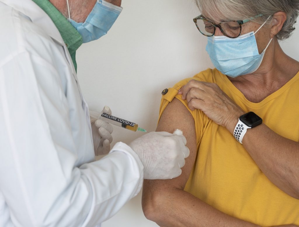 Coronavirus. Doctor injecting the covid-19 coronavirus vaccine to a senior woman in a yellow shirt