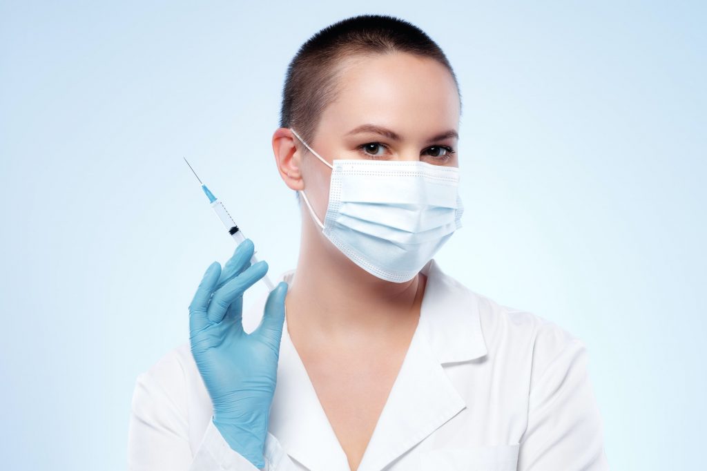 Short-haired woman doctor in mask holding syringe with medication